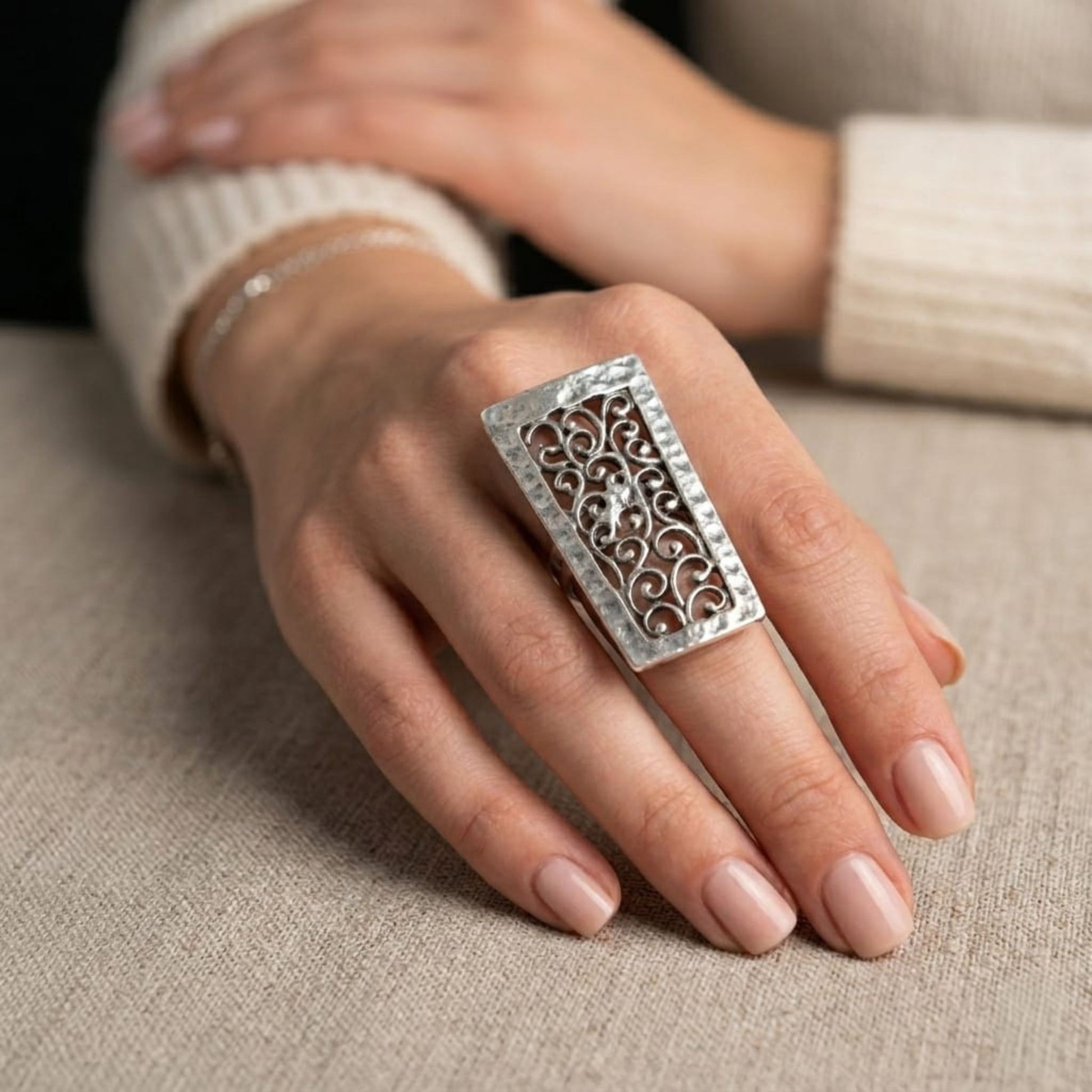 Modelo luciendo anillo Zamak rectangular con diseño de filigrana arabesca calada en plata envejecida, ajustable, Joyería Osnor Zamak