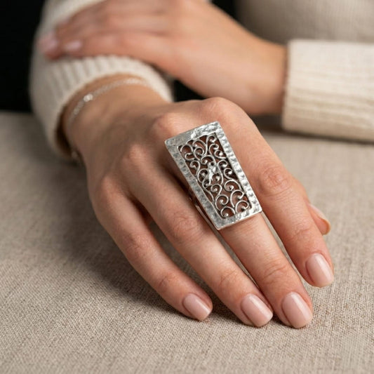 Modelo luciendo anillo Zamak rectangular con diseño de filigrana arabesca calada en plata envejecida, ajustable, Joyería Osnor Zamak