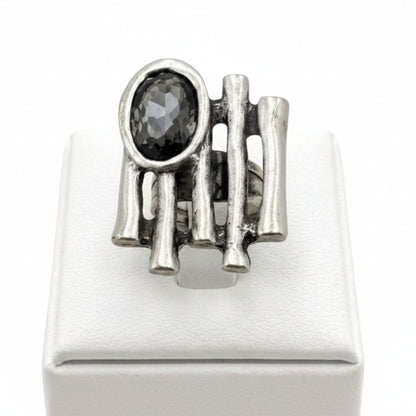 Anillo Zamak con circonita gris oscuro oval con varillas sobre expositor de madera, Joyería Osnor Zamak
