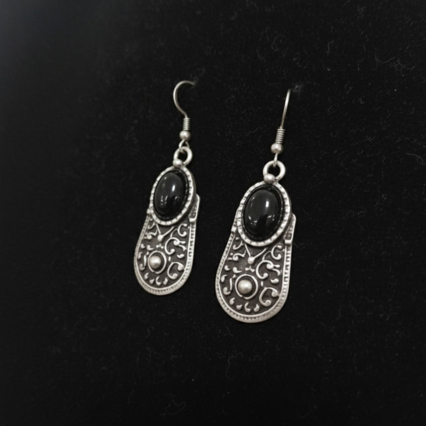 Pendientes de zamak con piedra negra, vista de detalle mostrando diseño calado y cierre gancho hippie hipoalergénico.
