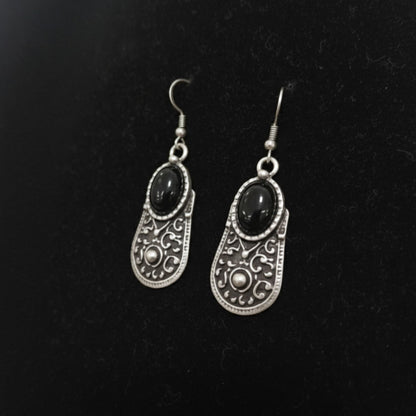 Pendientes de zamak con piedra negra, vista de detalle mostrando diseño calado y cierre gancho hippie hipoalergénico.
